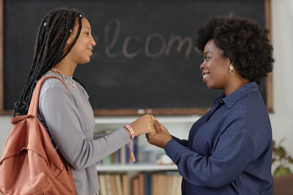 Smiling teacher holding hands with a student in front of a chalkboard that says Welcome
