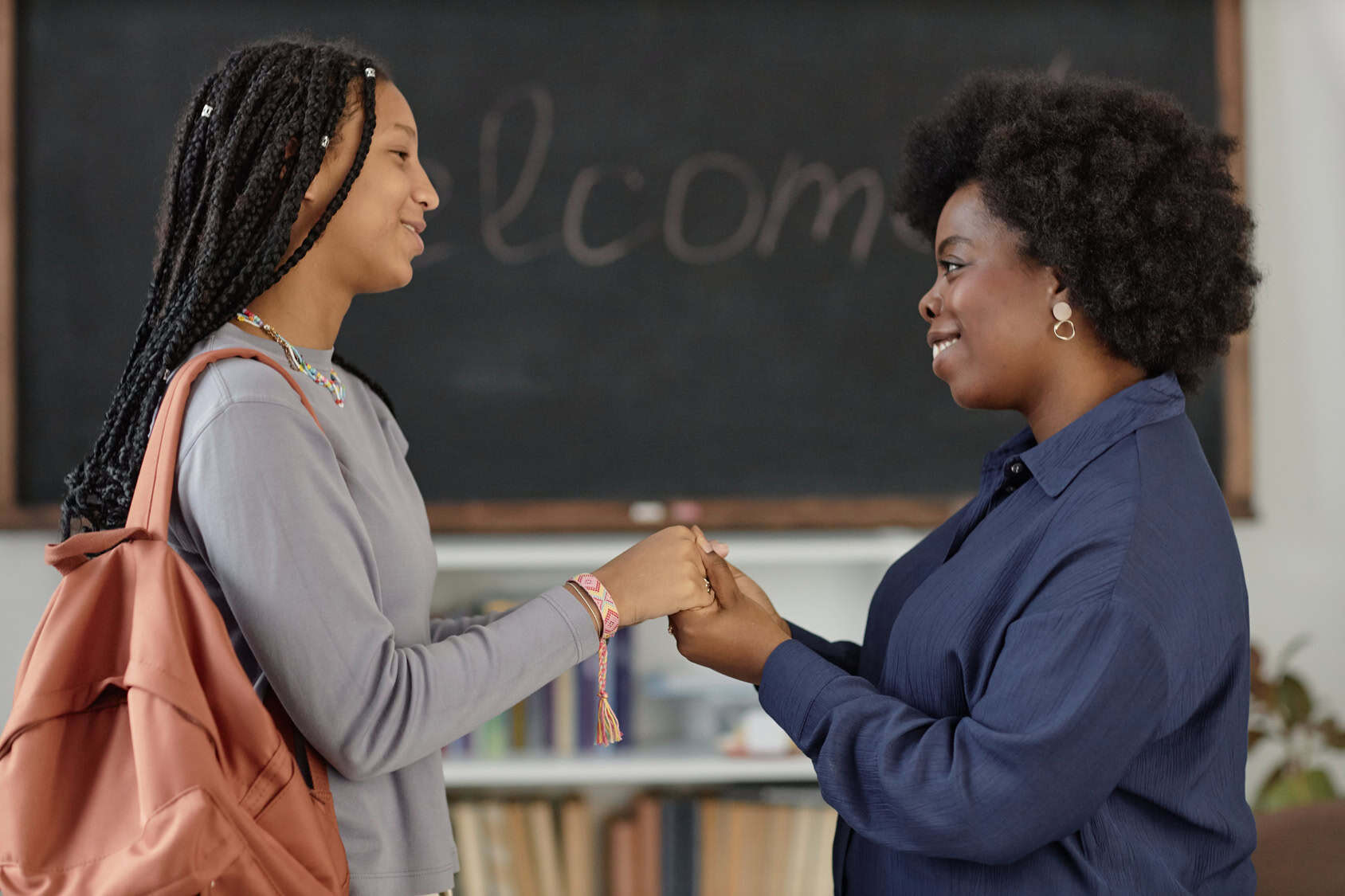 Smiling teacher holding hands with a student in front of a chalkboard that says Welcome